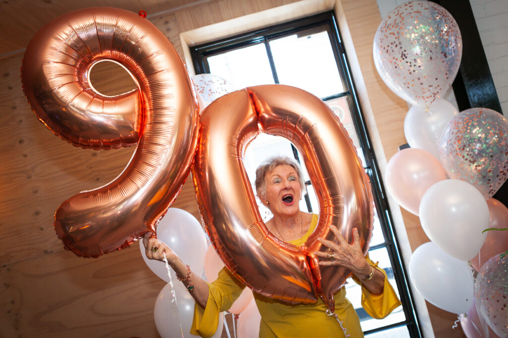 90 year old holds birthday balloons in shape of 9 0